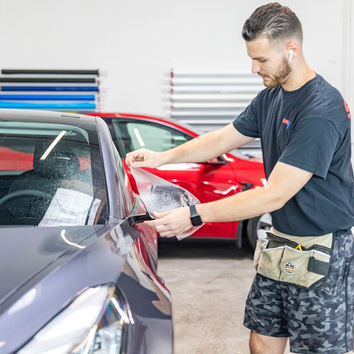 Man polishing a red car in an auto detailing shop, with a gray car in the foreground.