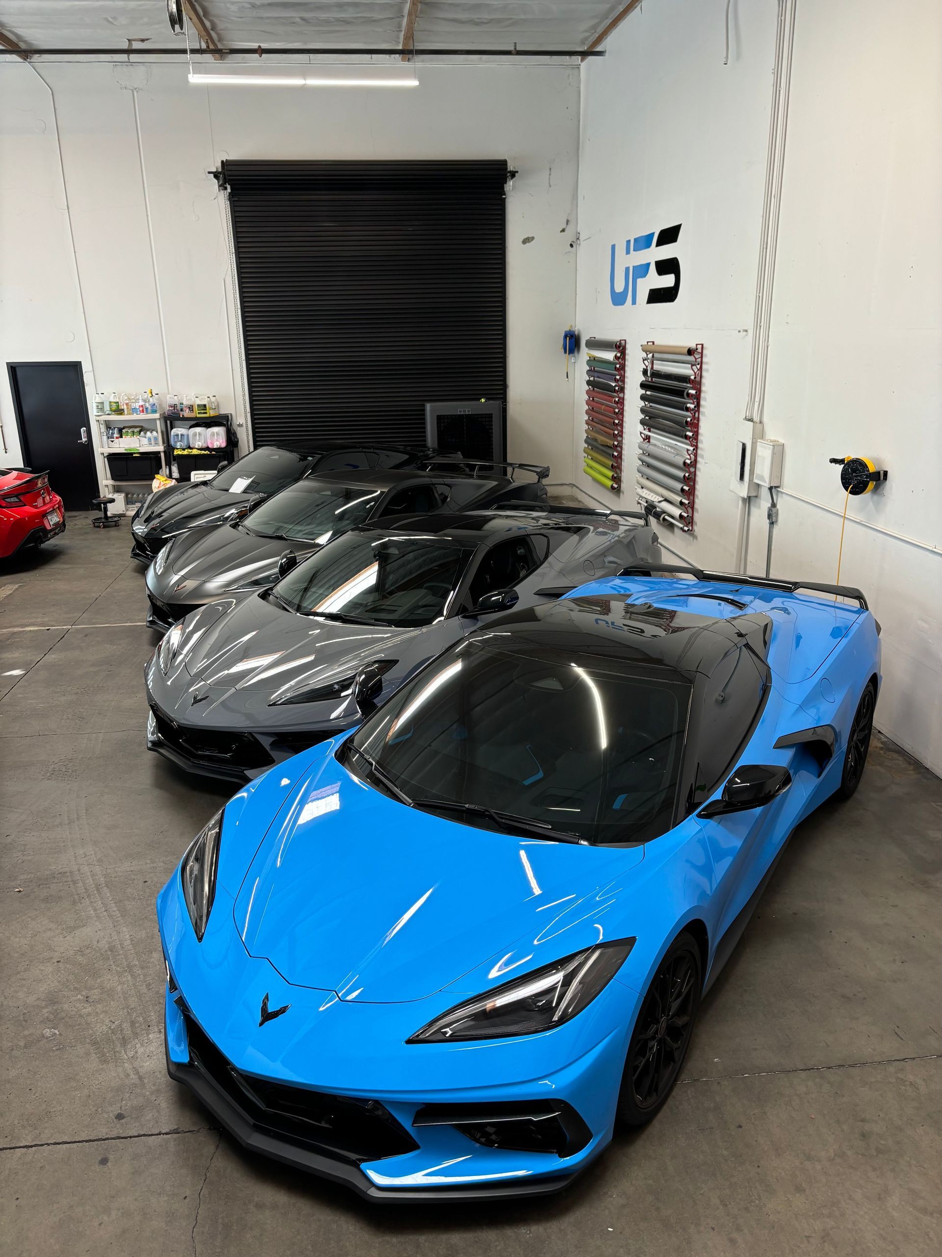 Blue sports car in a garage with two gray sports cars behind it