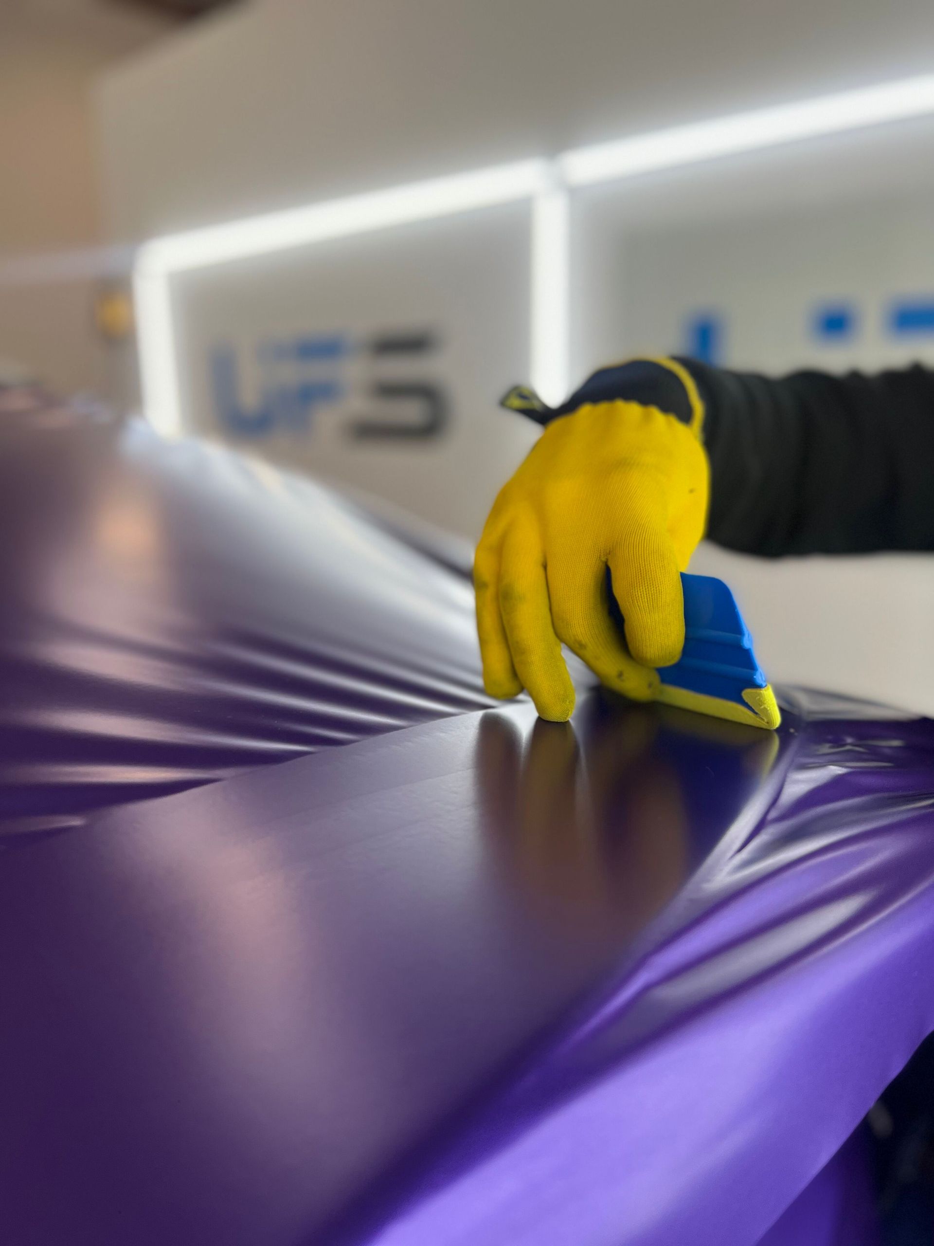 Gloved hand smoothing purple wrap film over a surface in a workshop