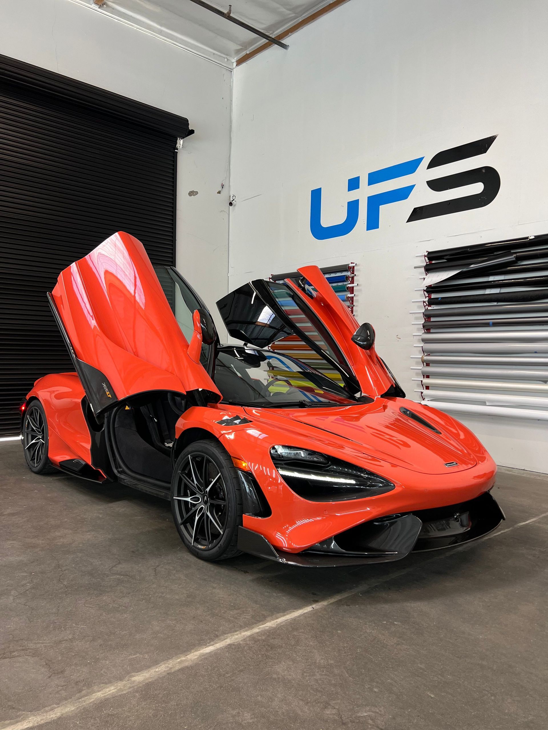 Bright orange sports car with scissor doors open in a showroom garage