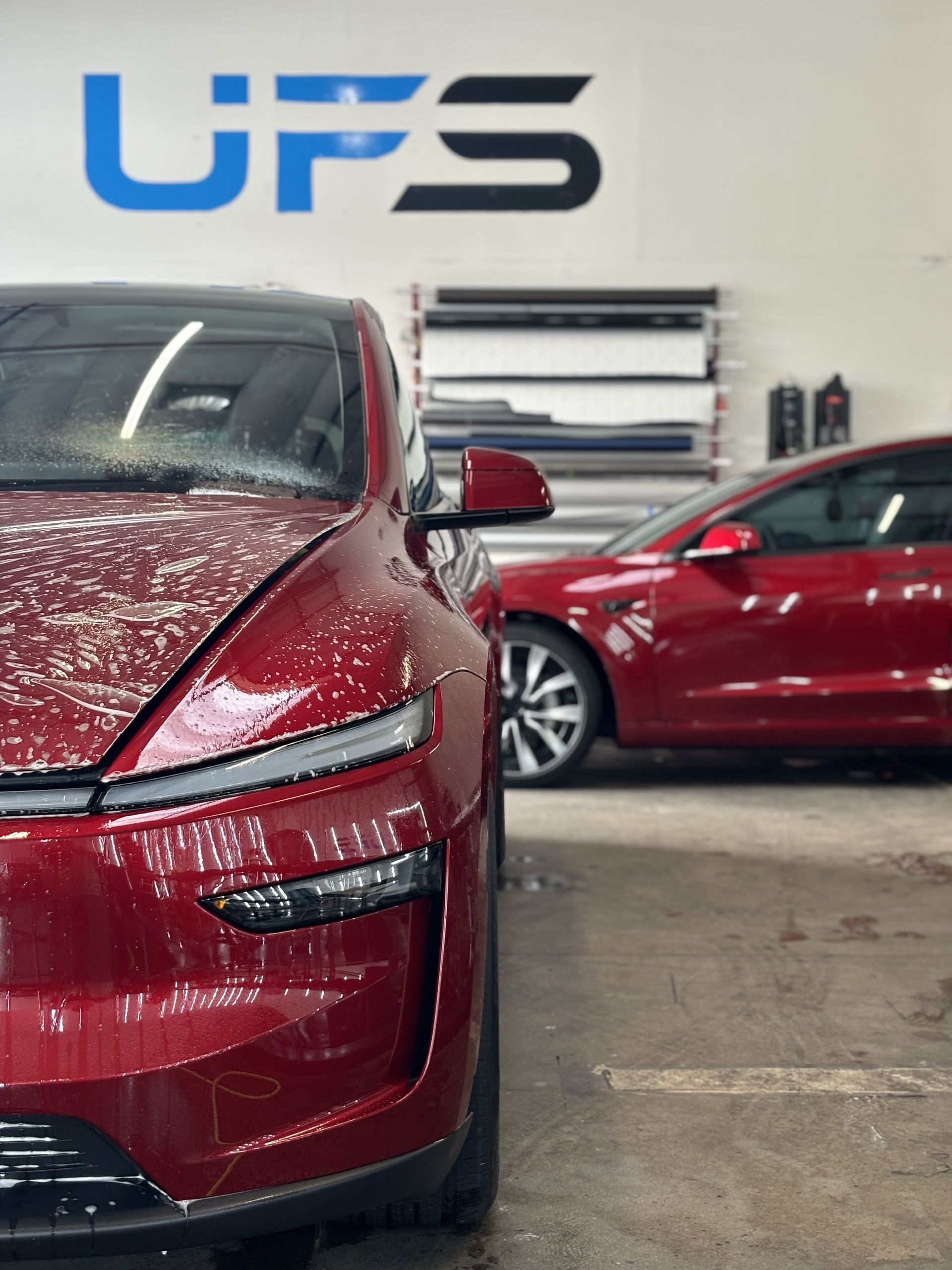 Two red cars in an indoor garage with a UPS sign on the wall