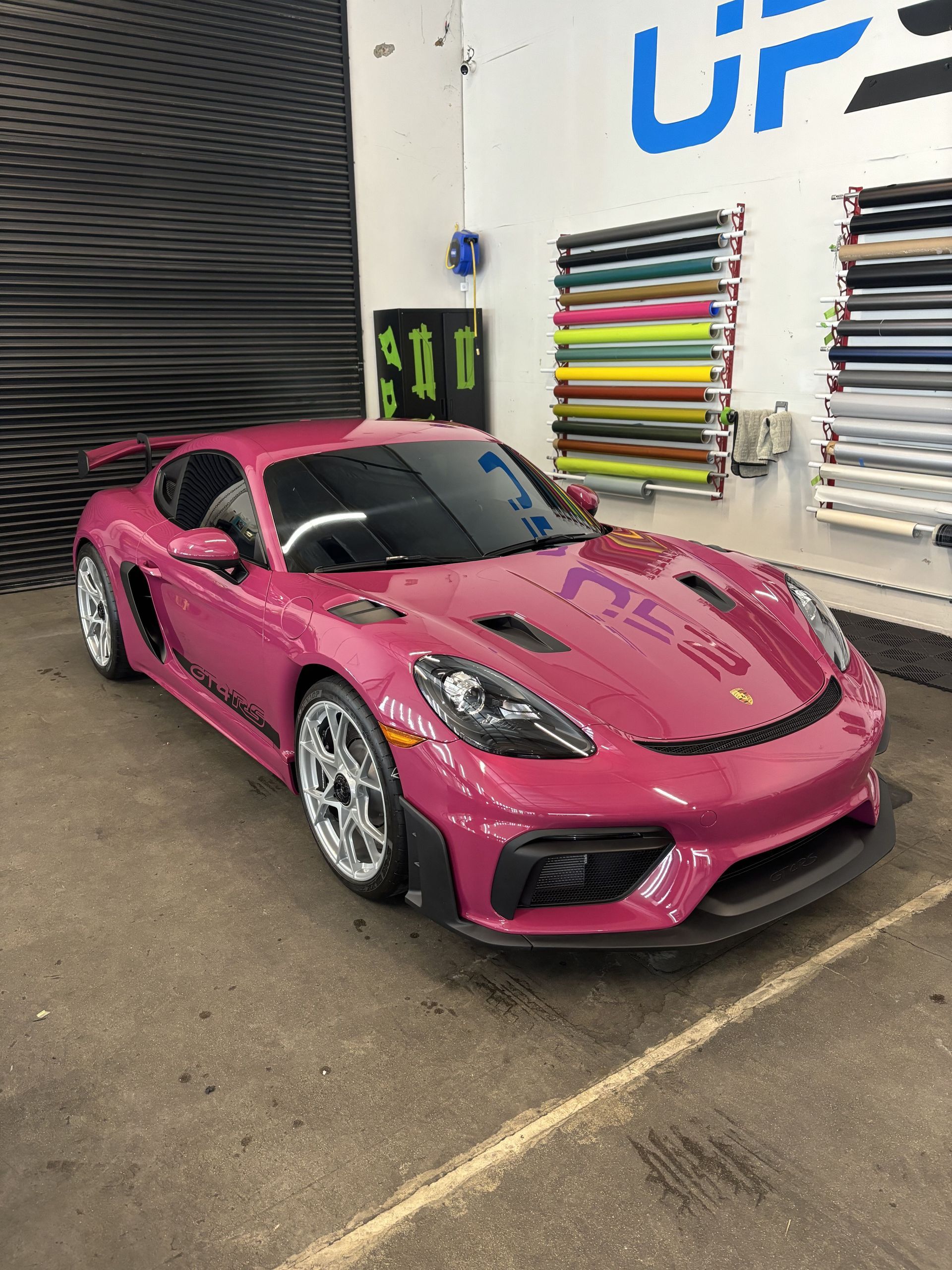 Pink sports car parked indoors beside wall-mounted tires and tools.