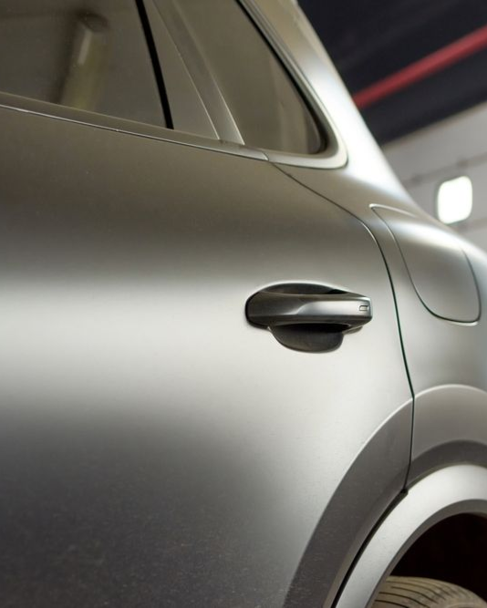 Close-up of a matte gray car door handle and rear quarter panel in a garage.