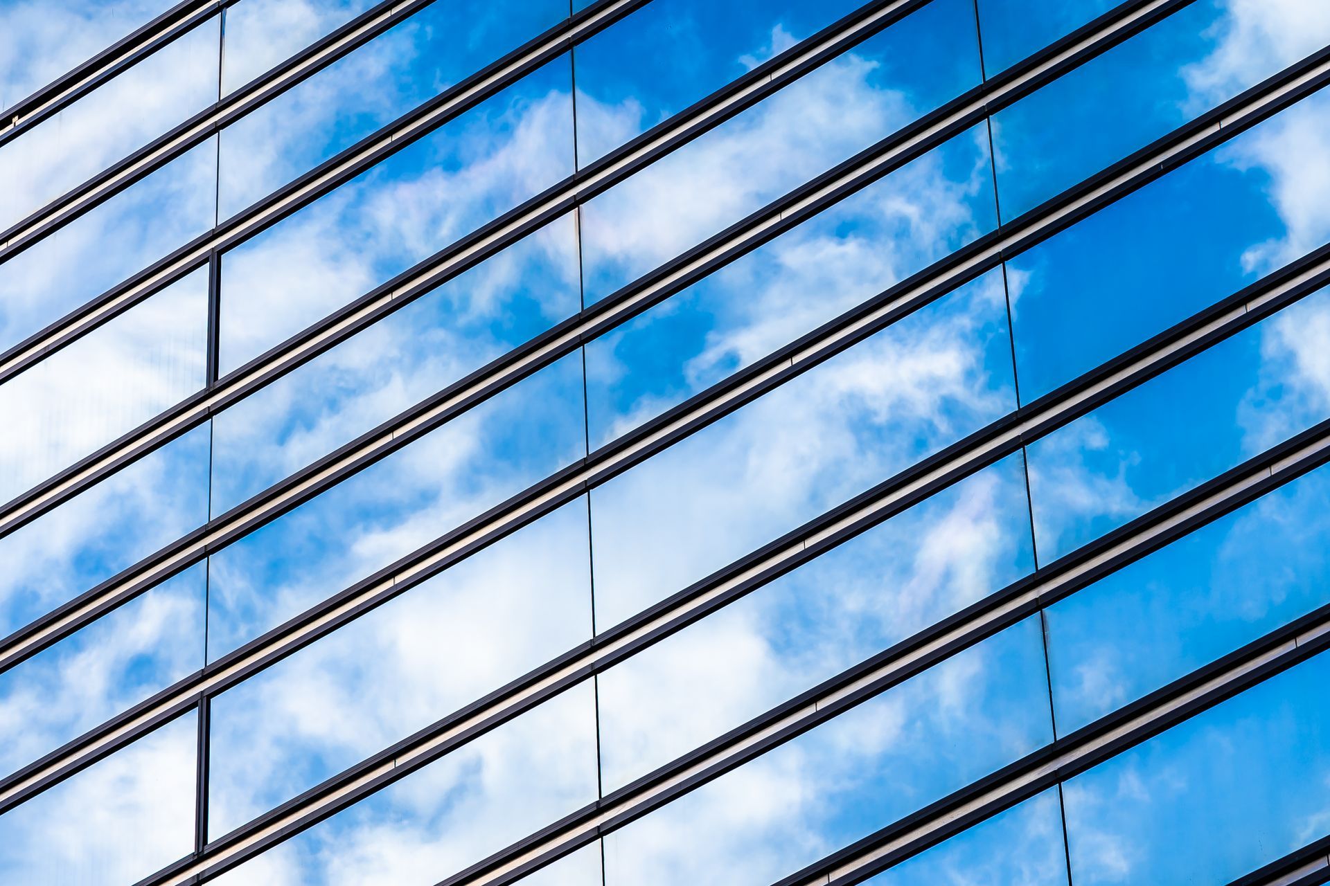 Diagonal glass building facade reflecting blue sky and clouds