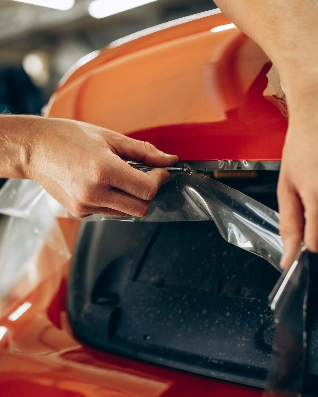 Hands installing clear plastic film on a red car bumper opening