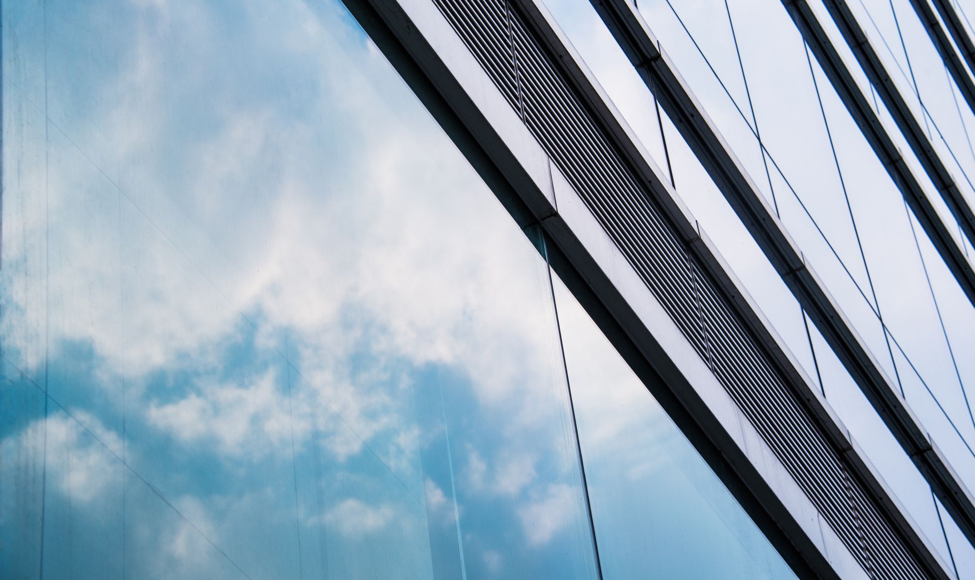 Skyscraper glass facade reflecting blue sky and clouds, with diagonal structural cables