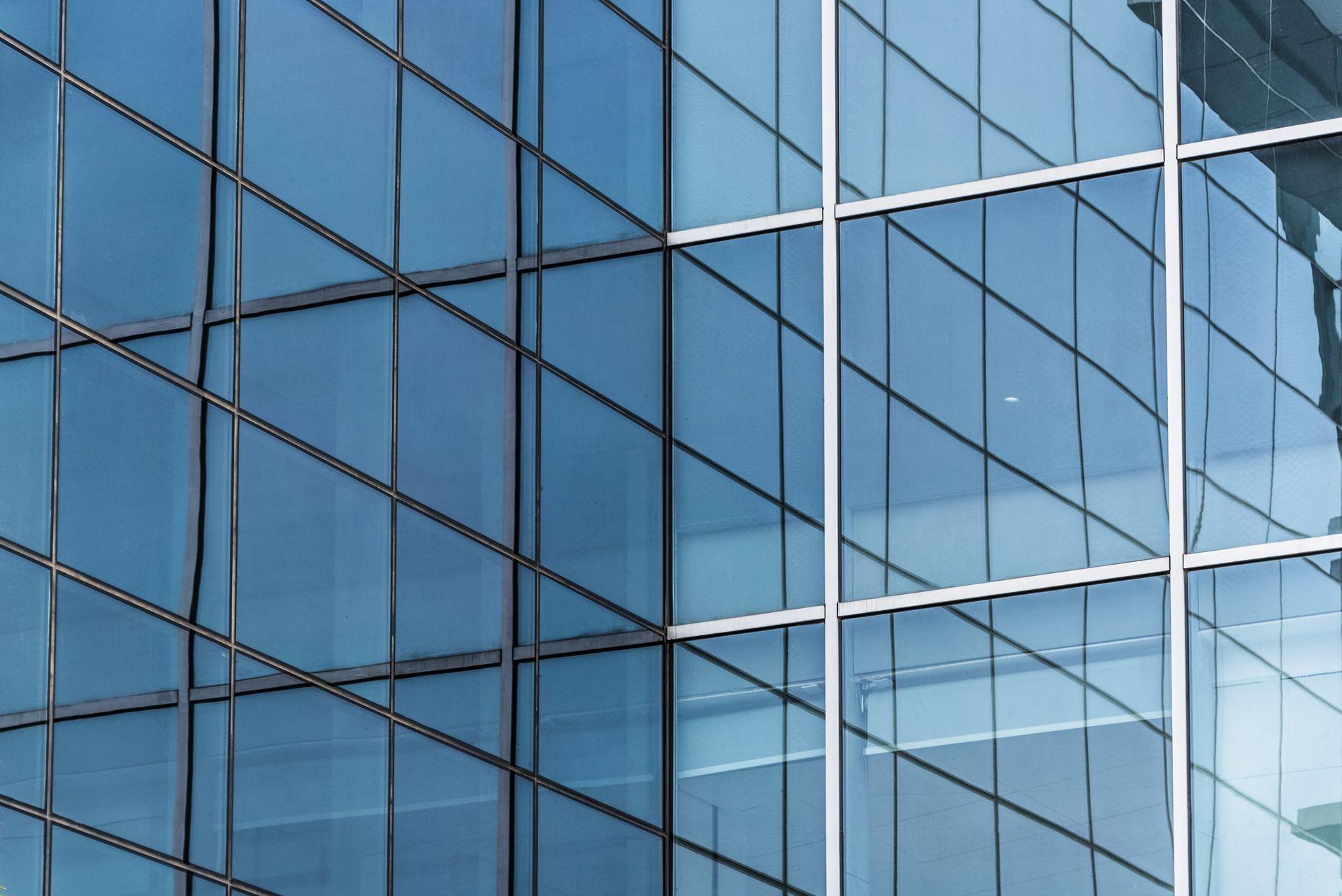Blue glass office building facade with reflective windows and white grid lines