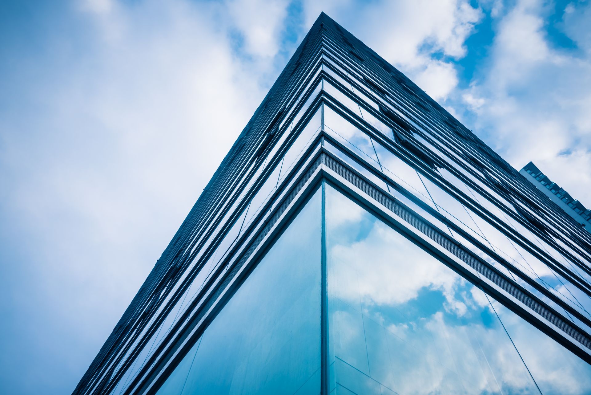 Glass skyscraper corner reflecting a blue sky with clouds