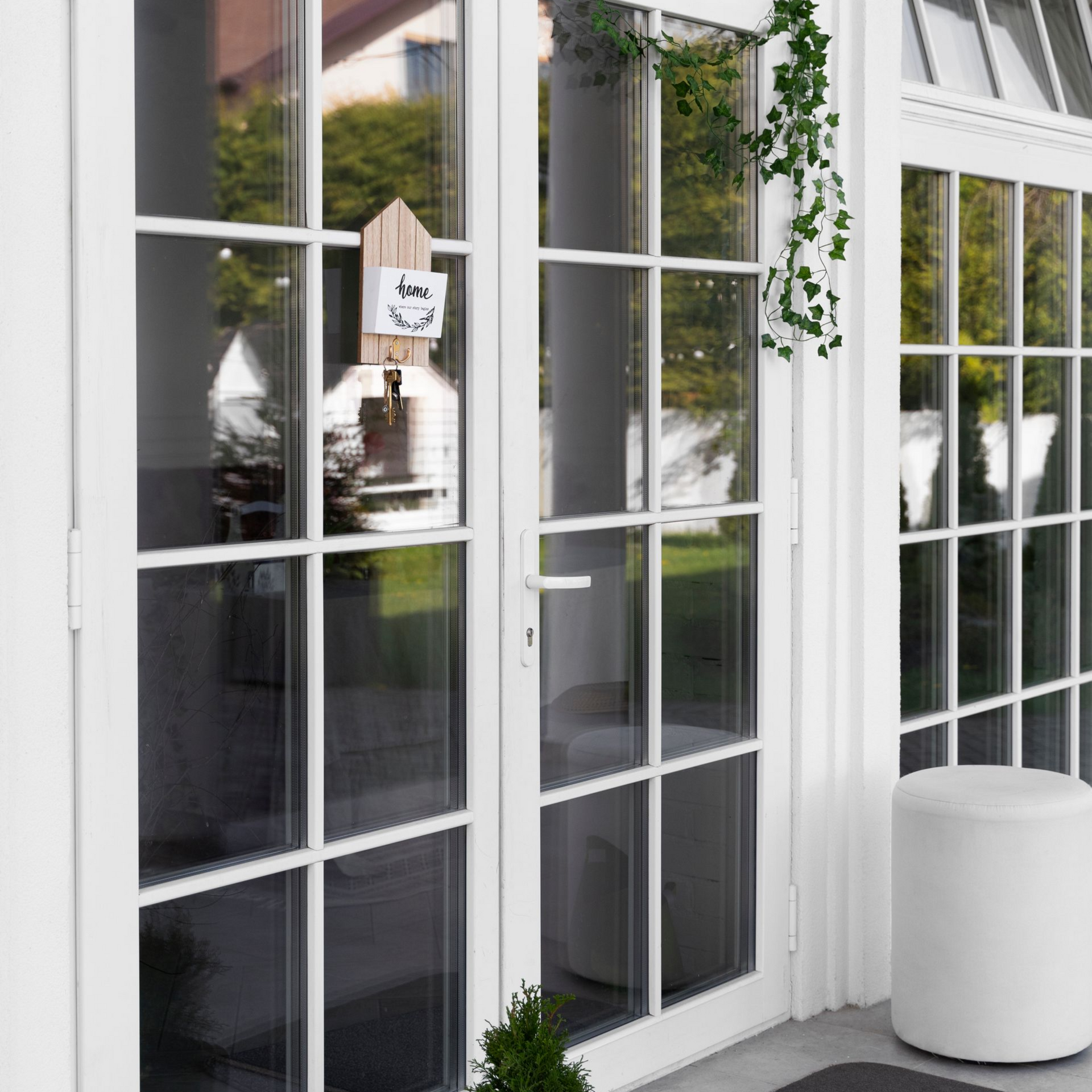 White French doors with glass panes opening to a patio, reflecting greenery and a hanging plant nearby