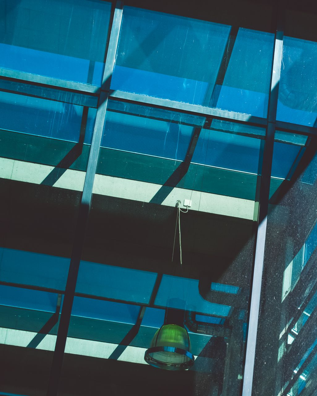 Blue-tinted glass skylight with a hanging light fixture and shadows inside a modern building