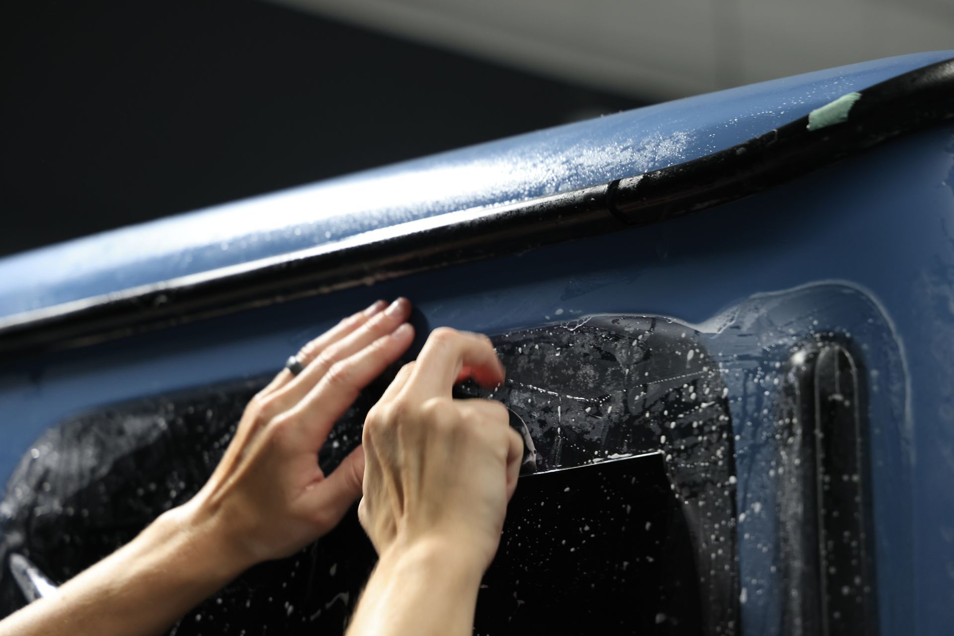 Hands polishing a wet black car roof with a cloth