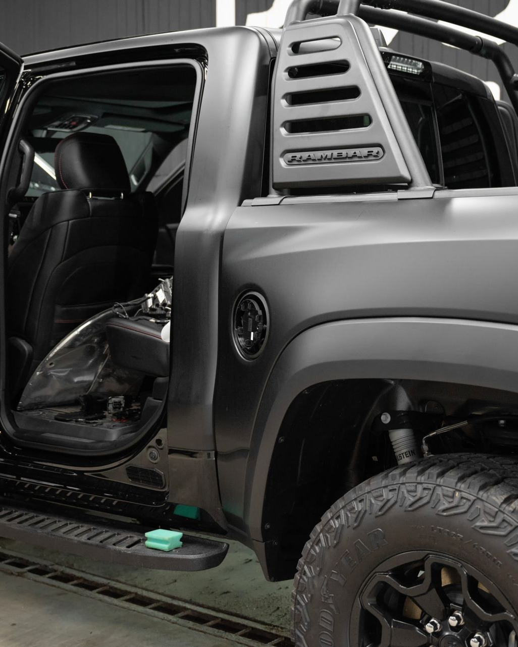 Black off-road truck with open rear door and side step, showing a glimpse of the dark interior.