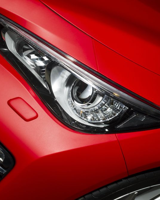 Close-up of a red car’s headlight and front fender.
