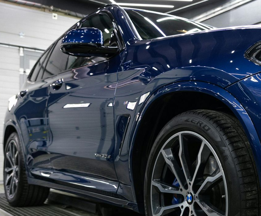 Gloved hand scrubbing a wet gray car hood with a blue brush