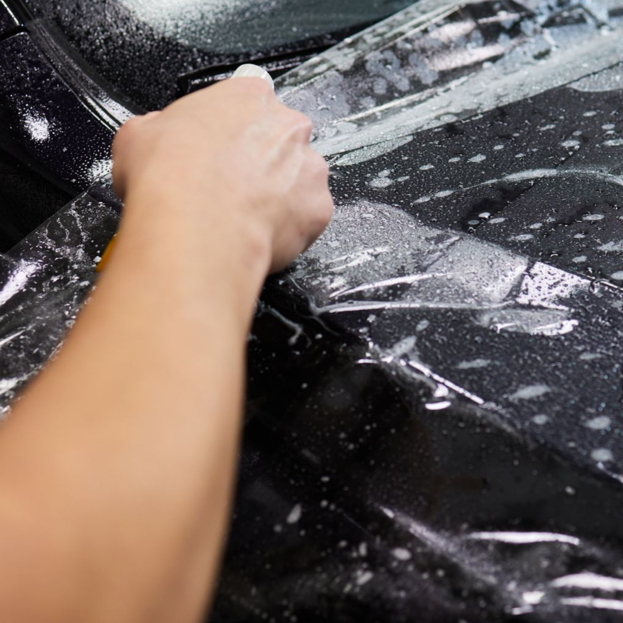 Hand washing a black car with soap suds on the windshield and hood