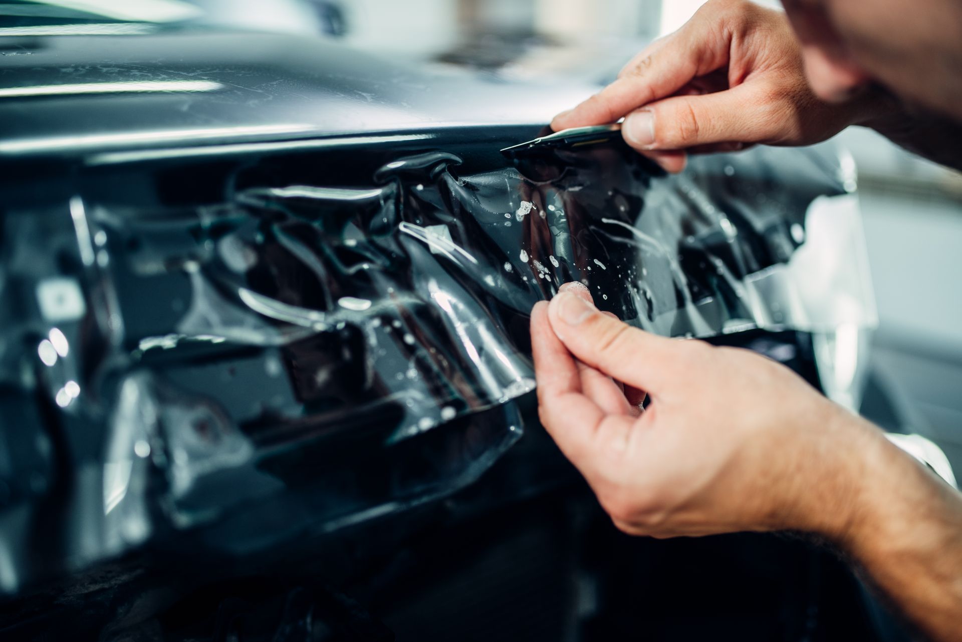 Hands peeling protective film from a car door panel in a workshop