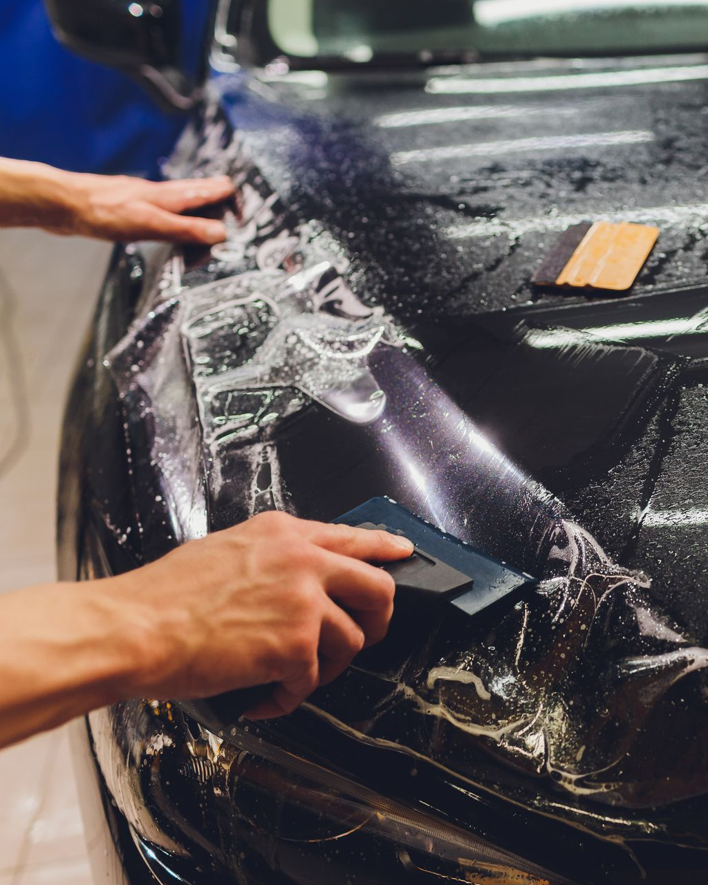 Person squeegeeing soapy water off a black car during a car wrap or tinting job