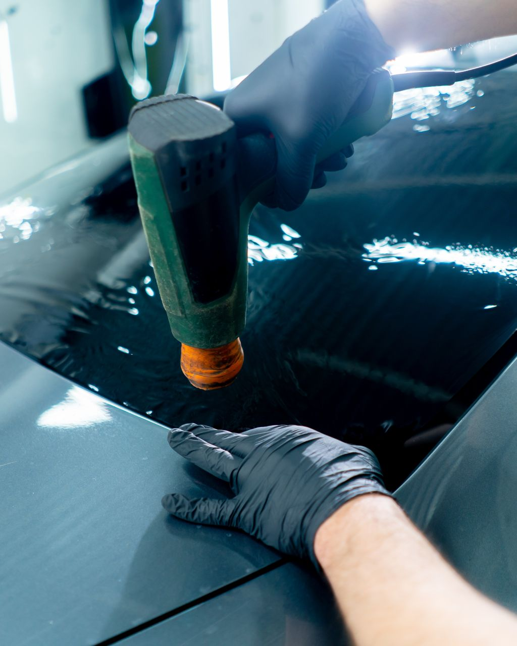 Two workers detailing a white SUV inside a garage, wiping the hood and windshield.