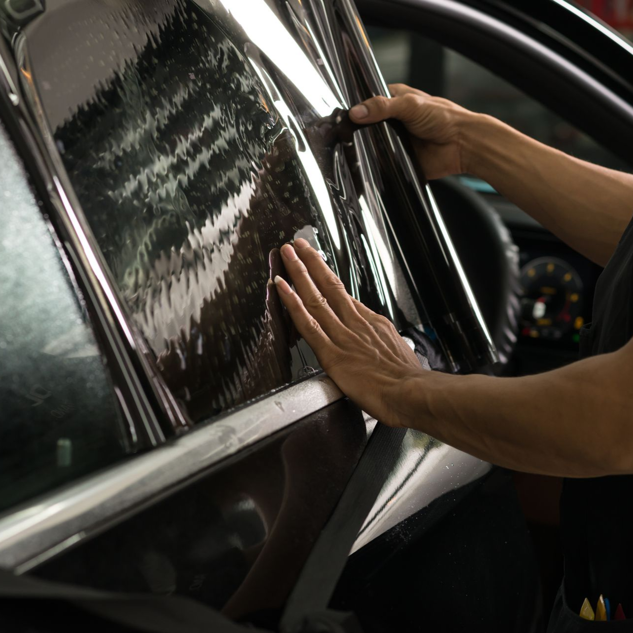 Hands wiping a black car's glossy window with a microfiber cloth.