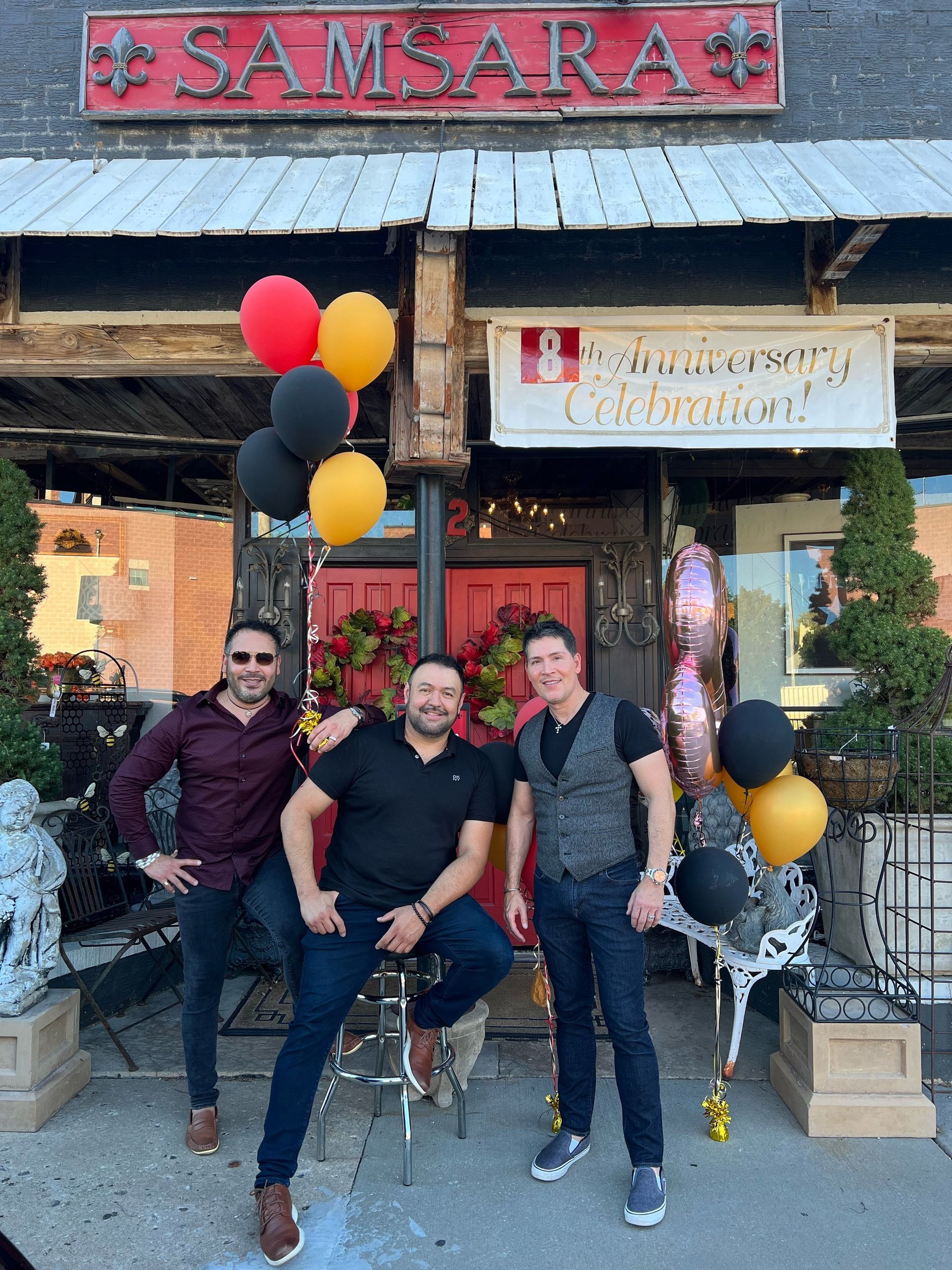 Three men are posing for a picture in front of a store called Samsara.