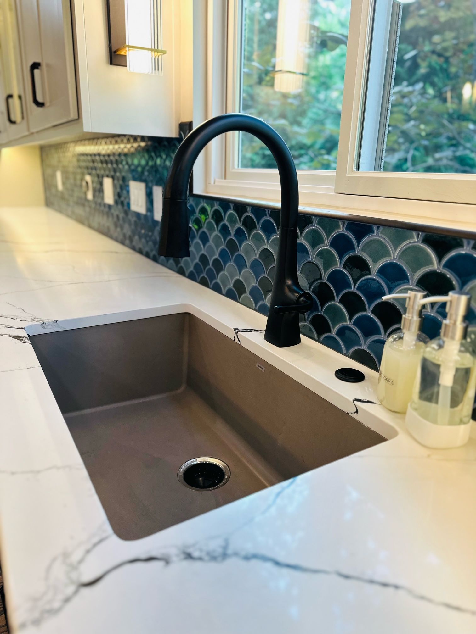 A kitchen sink with a black faucet and soap dispensers on the counter.