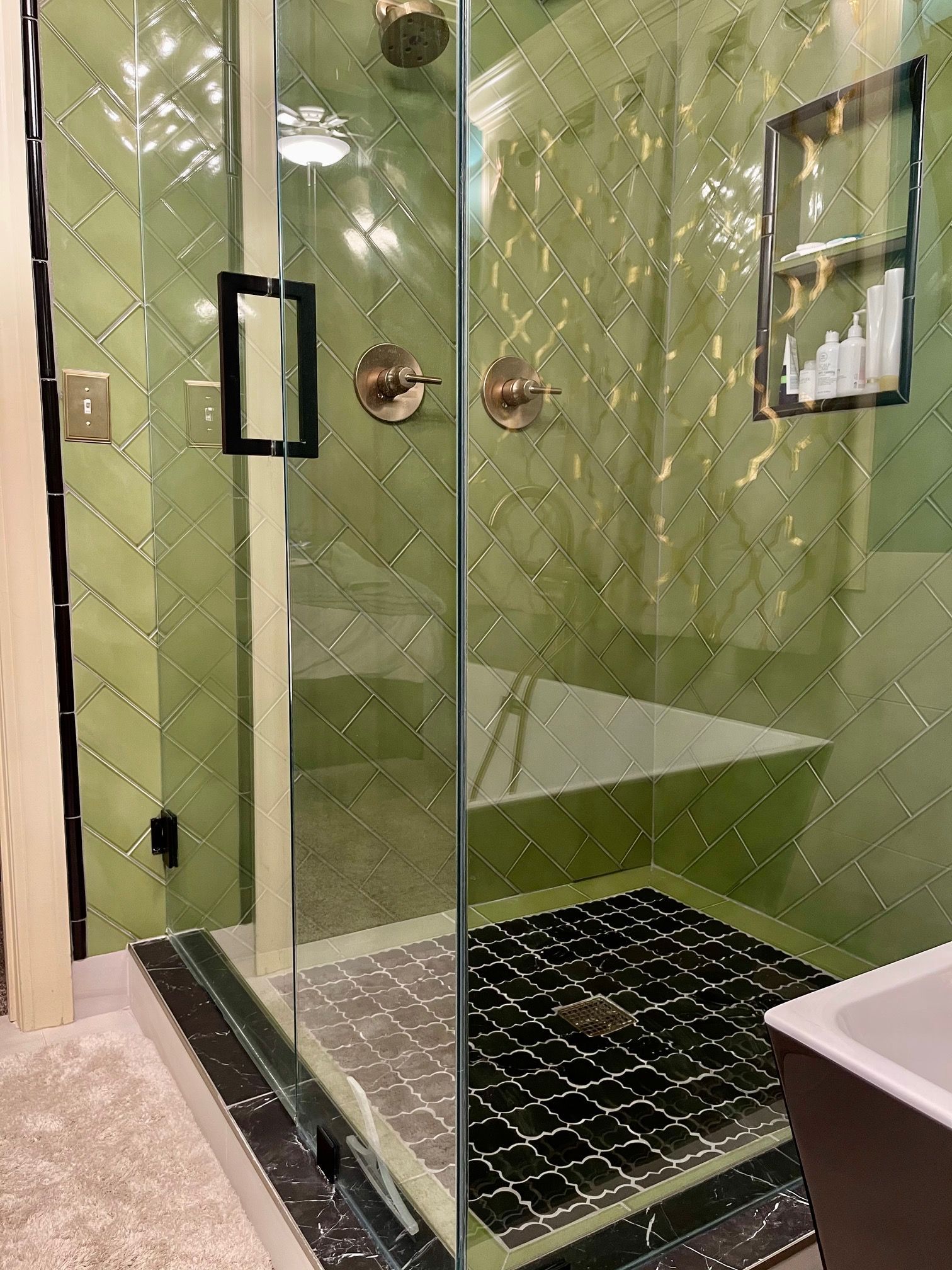 A bathroom with green tiles and a walk in shower with a glass door.