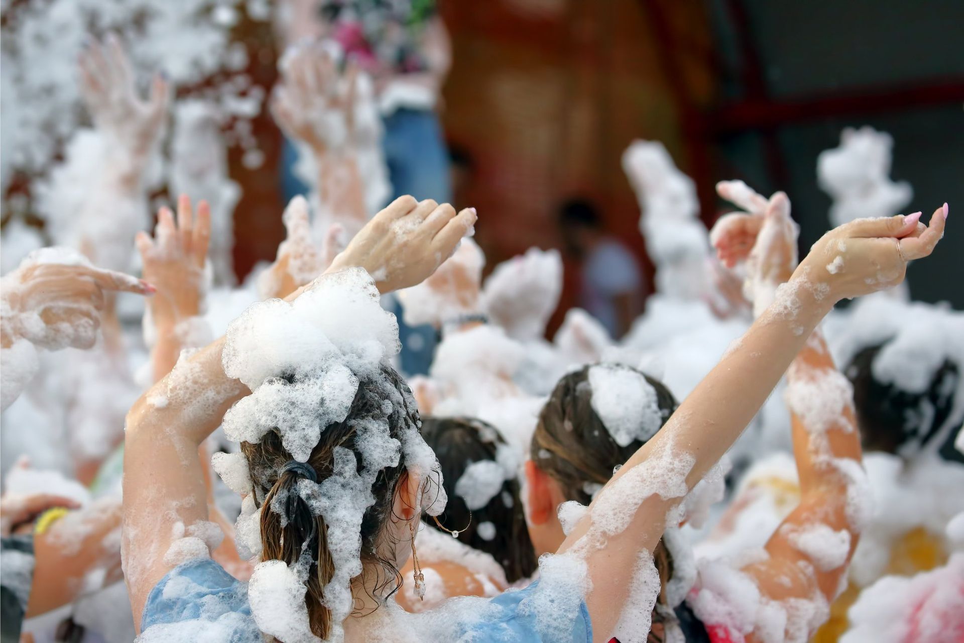 People with arms raised in a foam party, enjoying themselves.