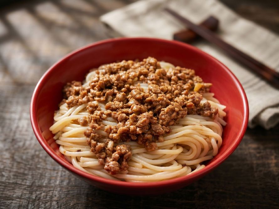 Red bowl of spaghetti topped with meat sauce on a rustic wooden table