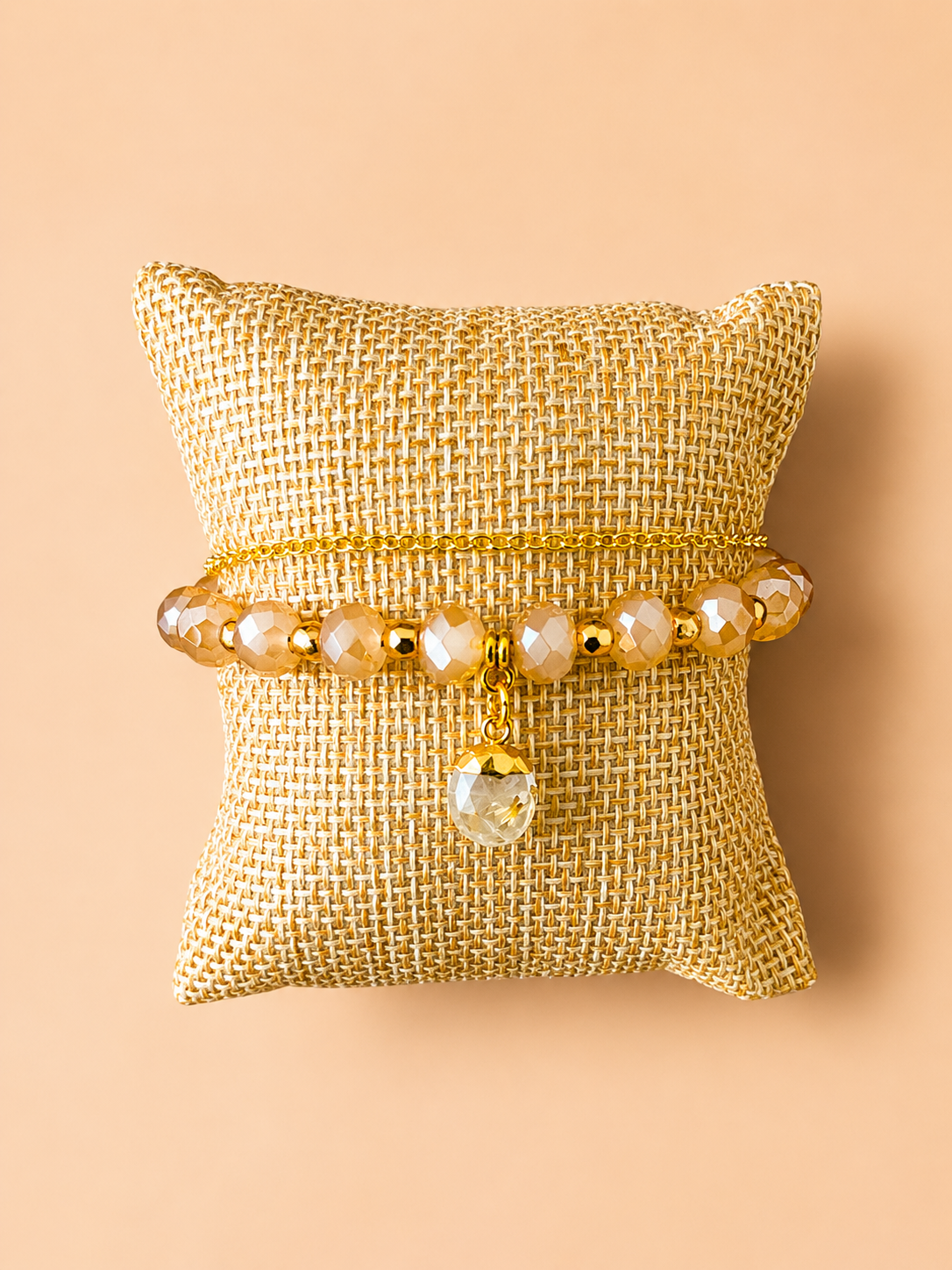 Gold beaded bracelet on a cream fabric pillow, centered on a beige background