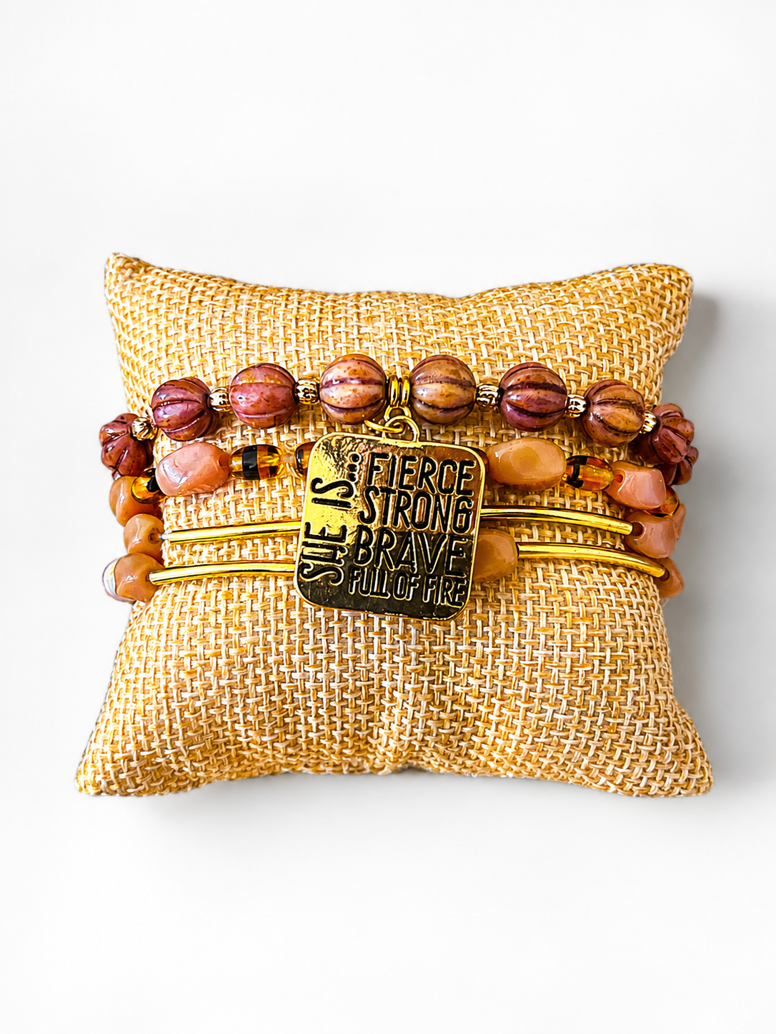 Beaded gold-toned cuff bracelet on a textured beige cushion