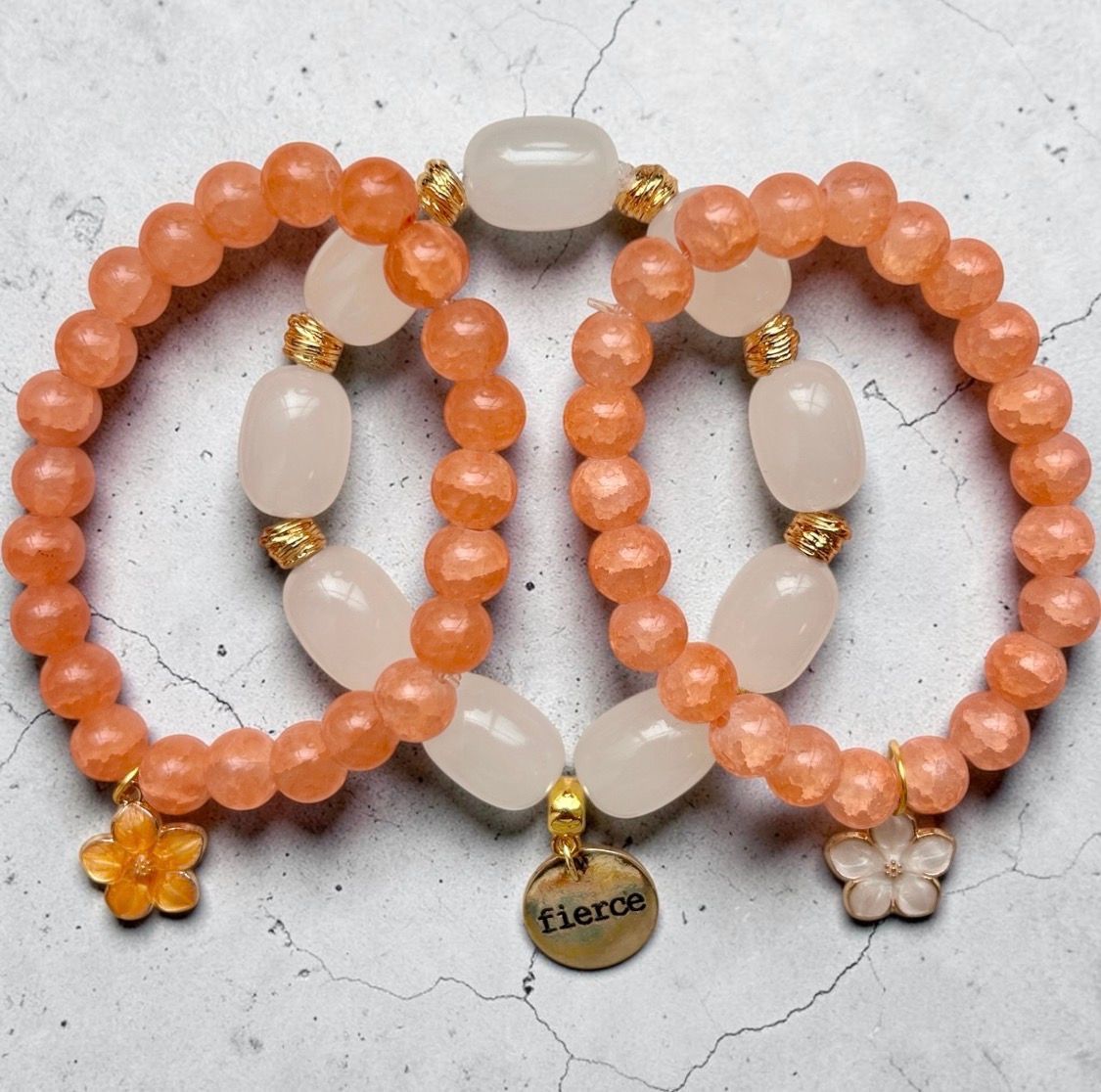 Two coral and white beaded bracelets with flower charms on a light fabric background