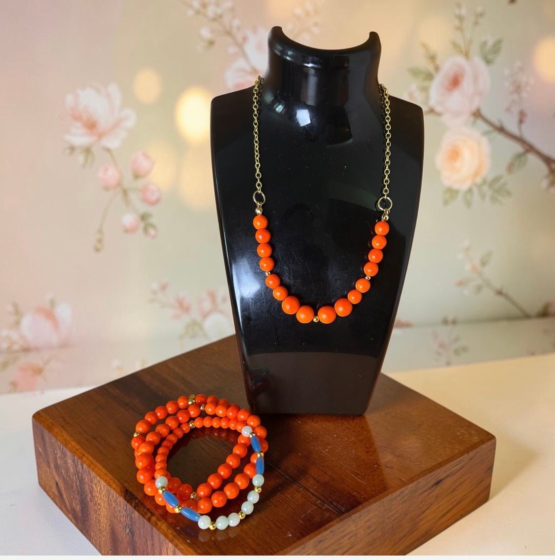 Orange beaded necklace and matching bracelet displayed on a black bust and wooden stand