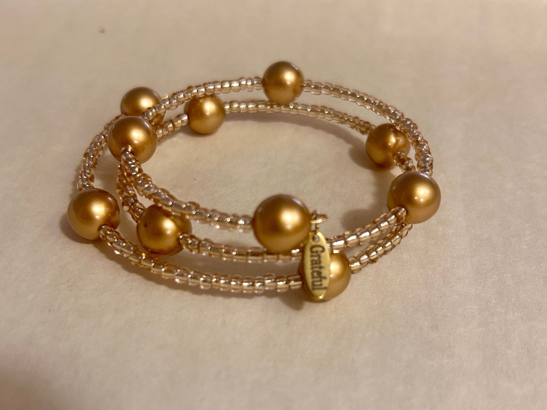 Gold beaded bracelet with pearl-like strands and round gold beads on a neutral background