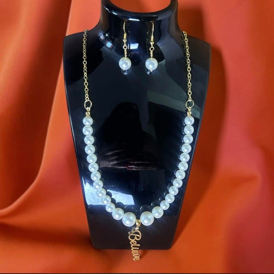 Black necklace display bust with pearl necklace and matching pearl earrings on red fabric background