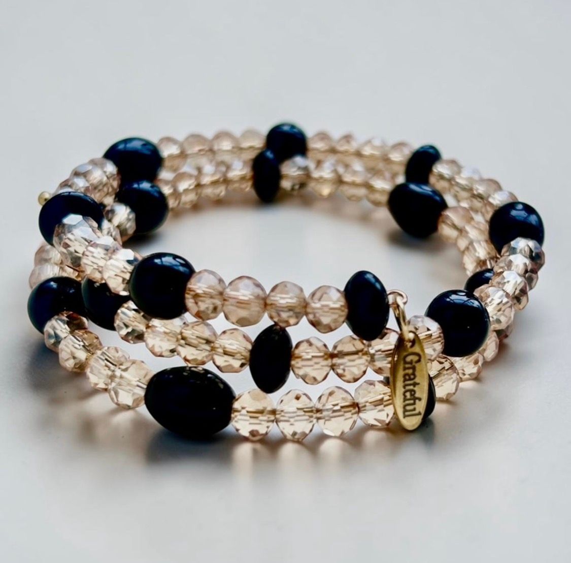 Three stacked beaded bracelets with gold and black beads on a white background