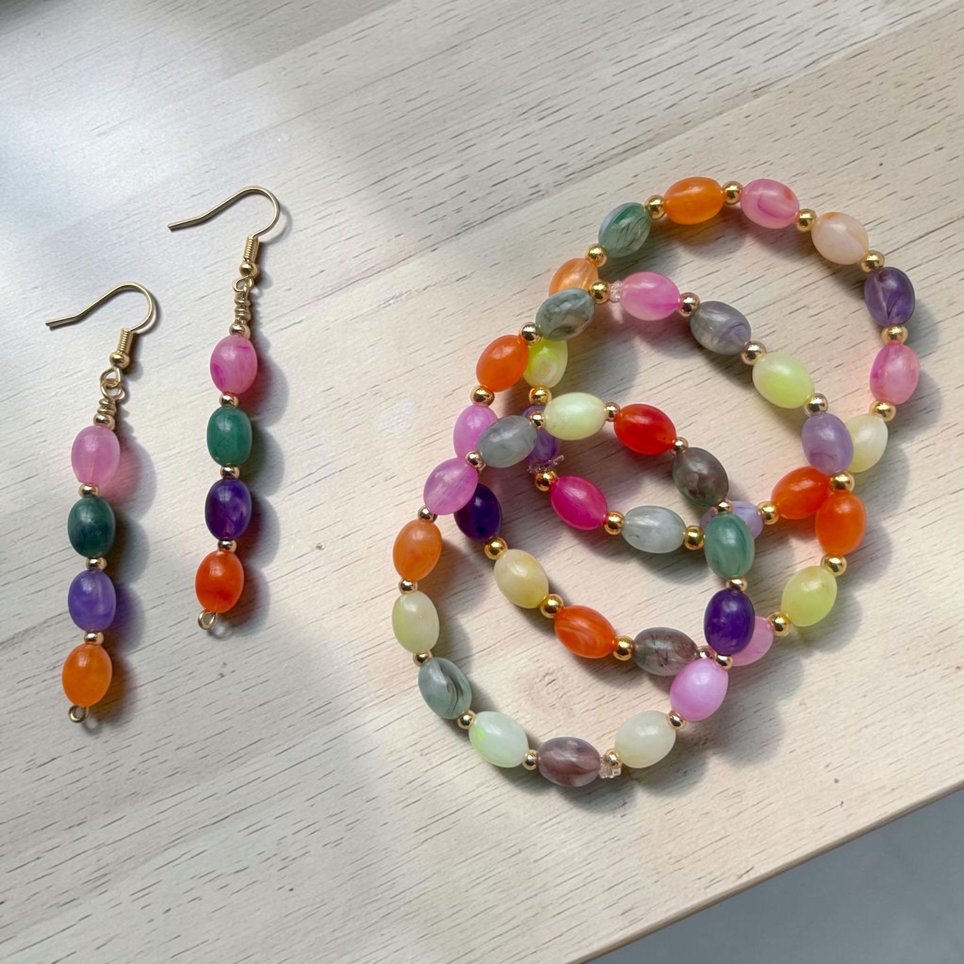 Pastel beaded bracelet and matching drop earrings on a textured white surface