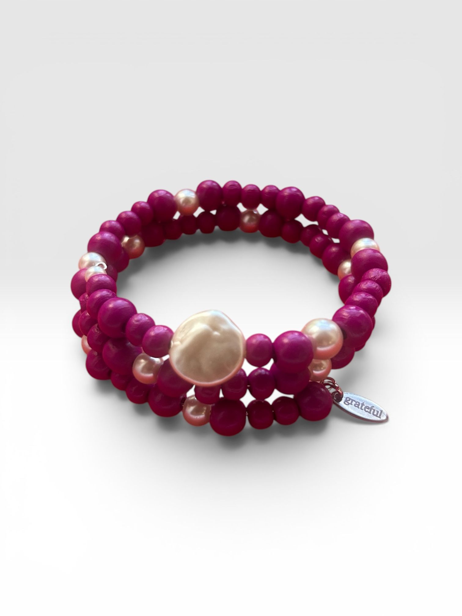 Magenta beaded bracelet with a large pearl centerpiece on a white background