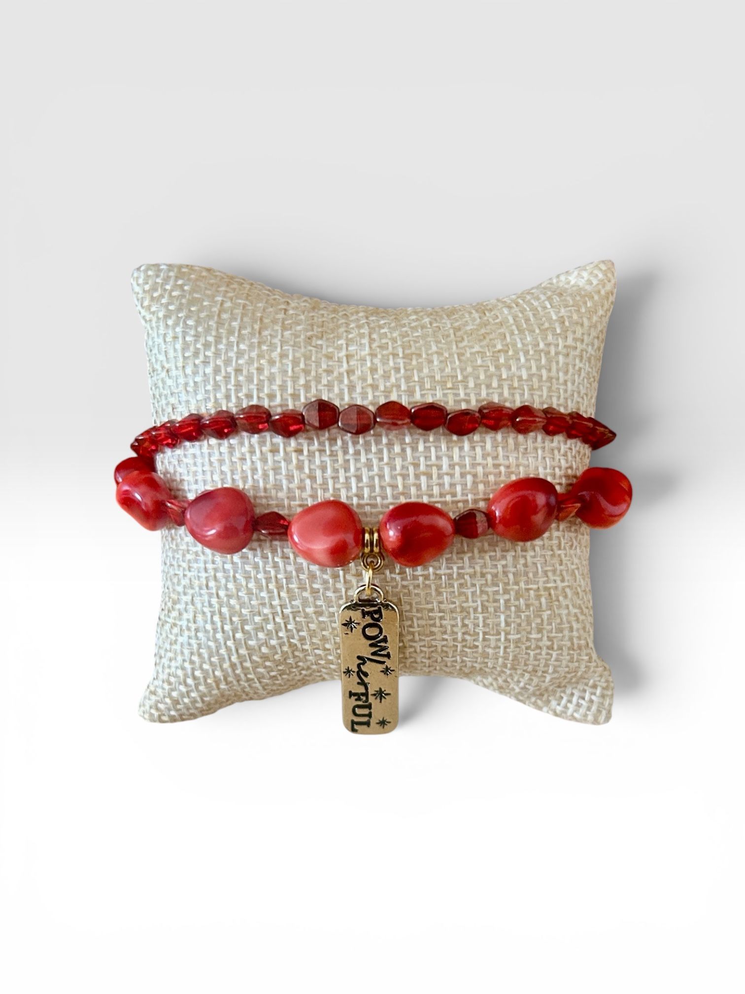 White textured pillow with red beaded bracelets wrapped around it and a small hanging tag