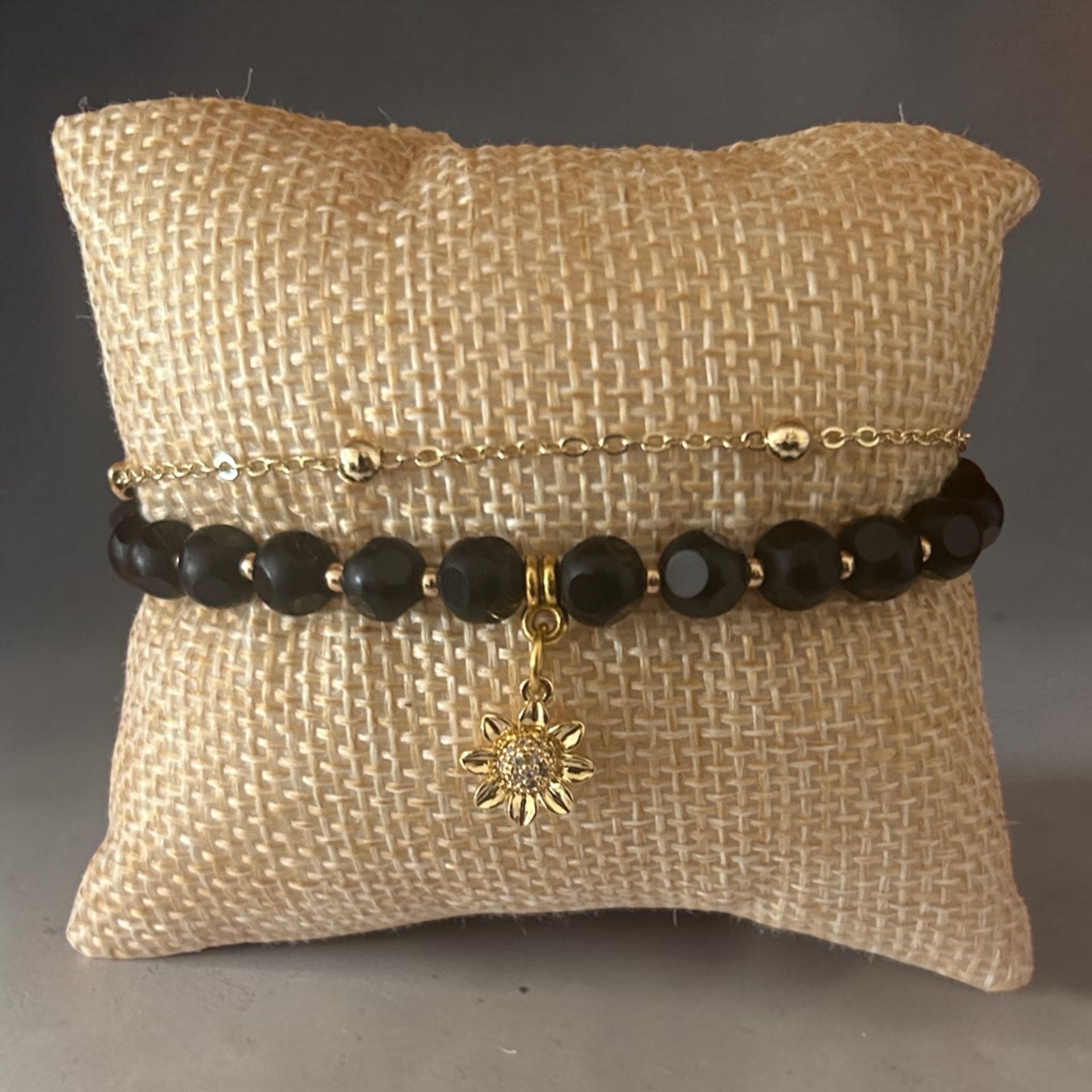 Beige burlap pillow with black bead bracelets and a gold star charm