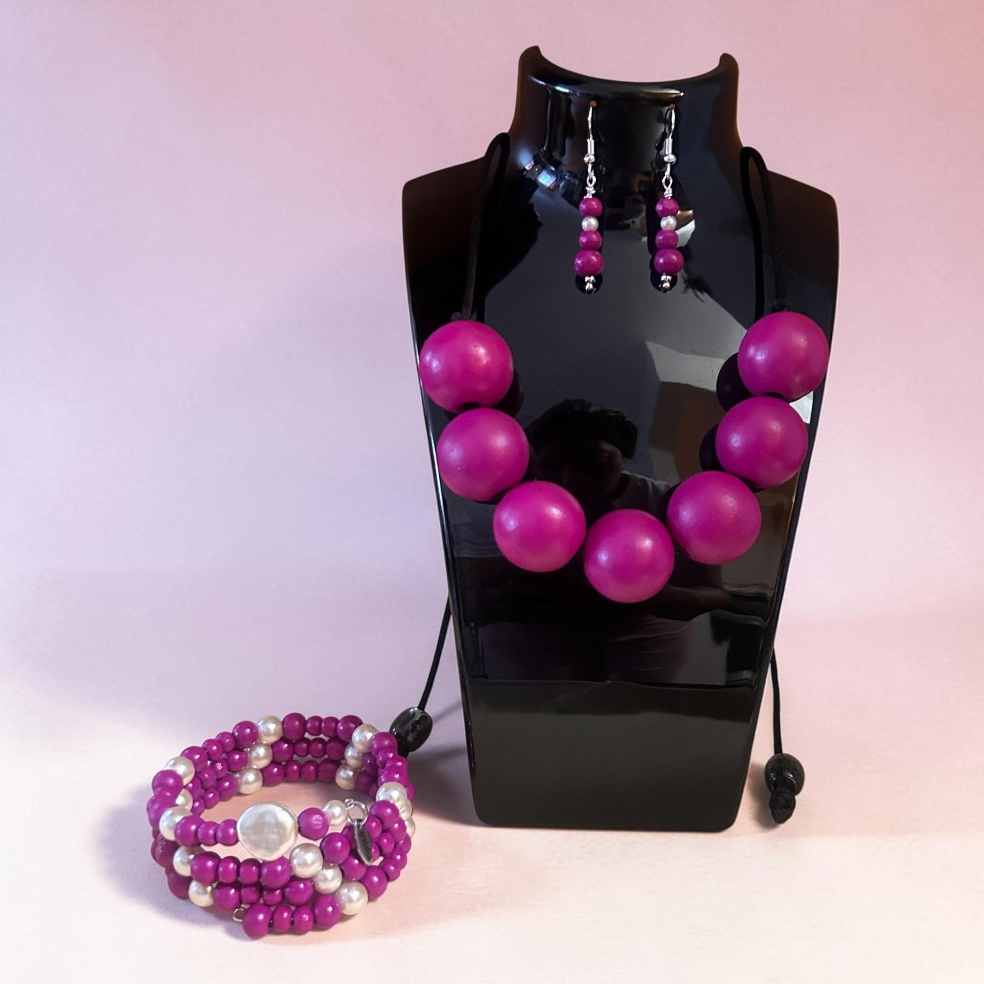 Black display bust with magenta beaded necklace, dangling earrings, and matching bracelet on a white background