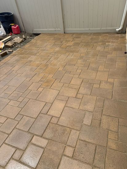 Tan and brown stone pavers laid in a multi-sized, interlocking rectangular pattern on a residential patio.