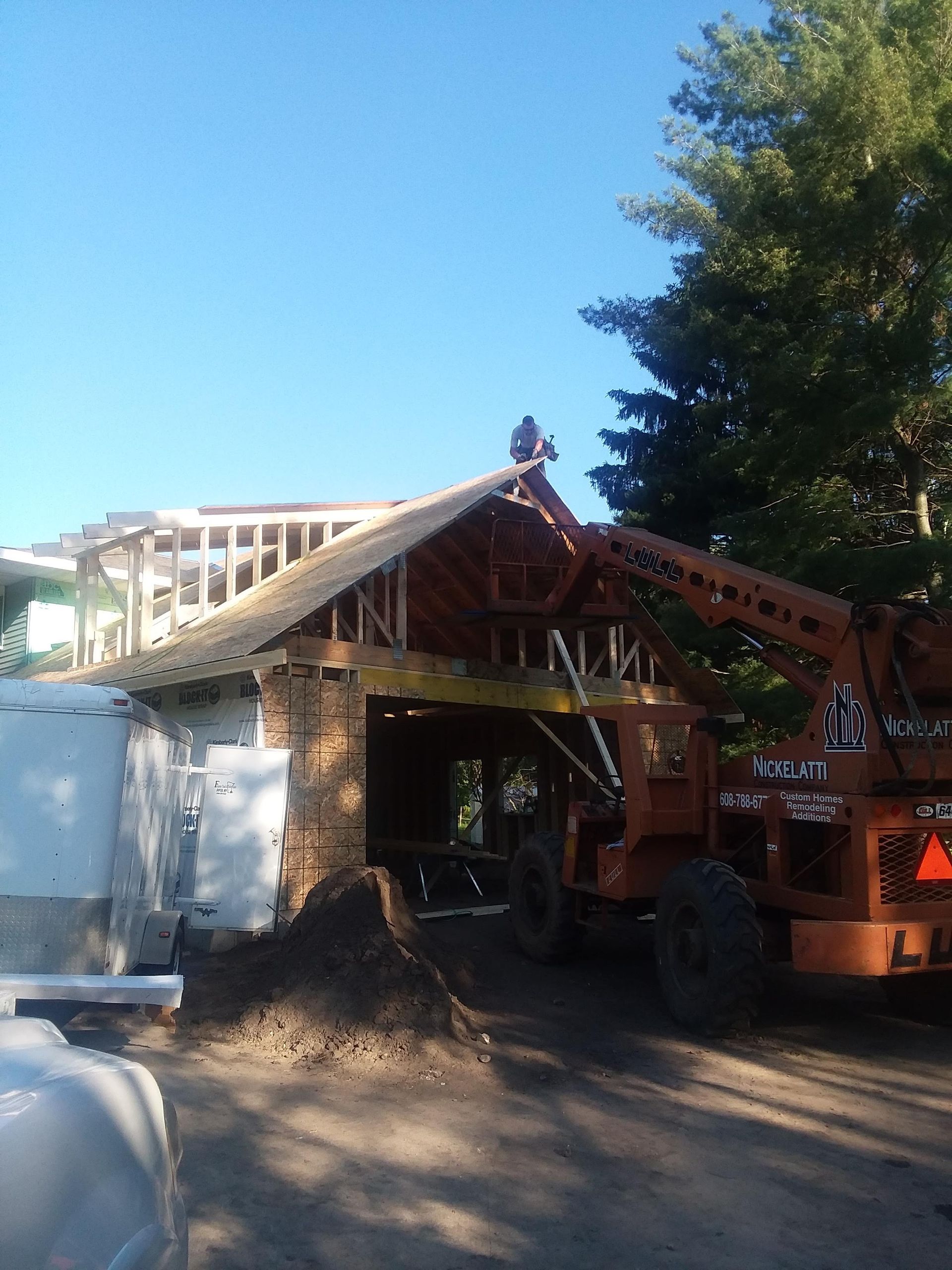 Damaged wooden house frame on a construction site with a crane and trees nearby