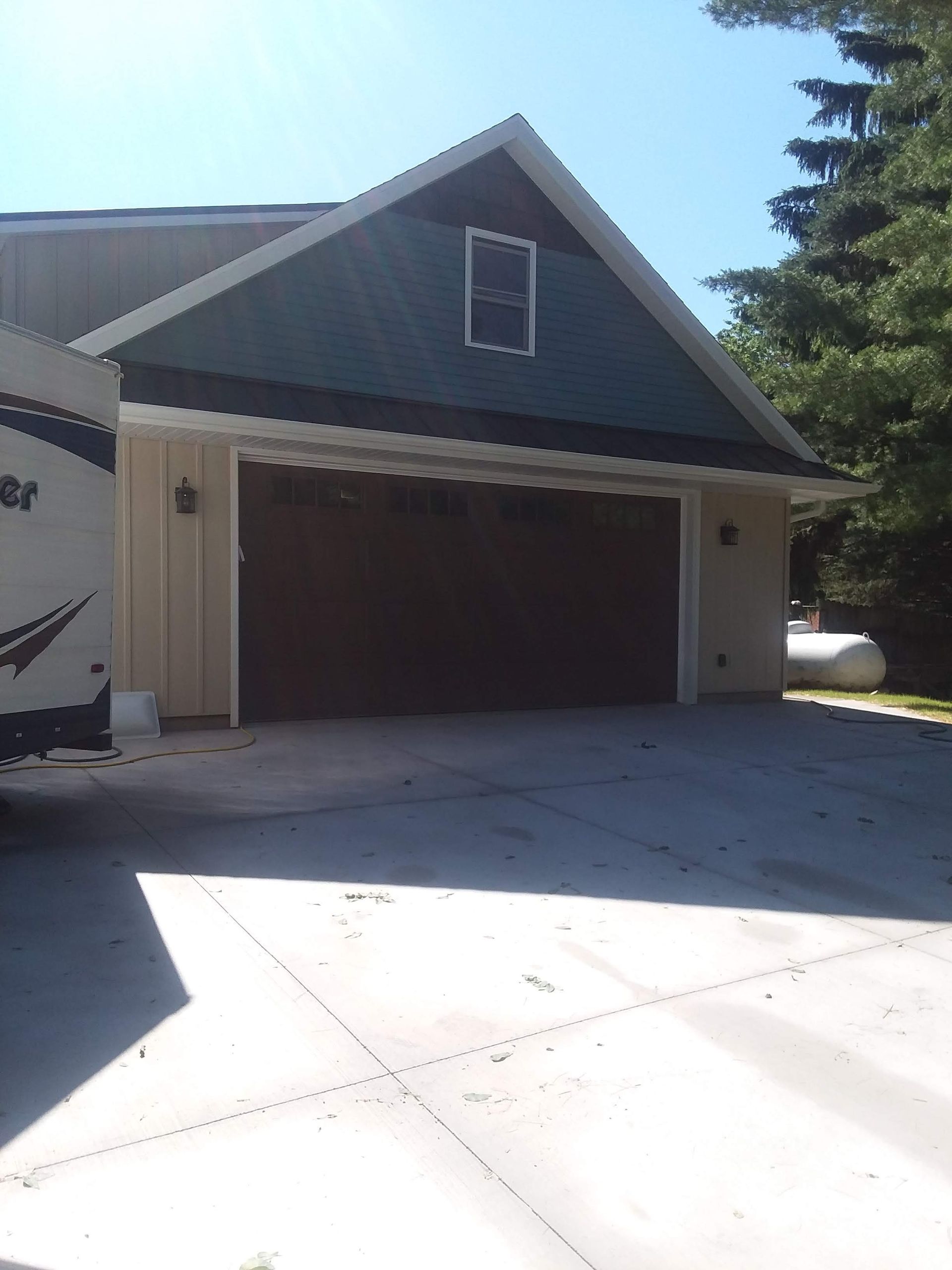 Detached garage with brown doors, gray siding, and a concrete driveway under a clear blue sky