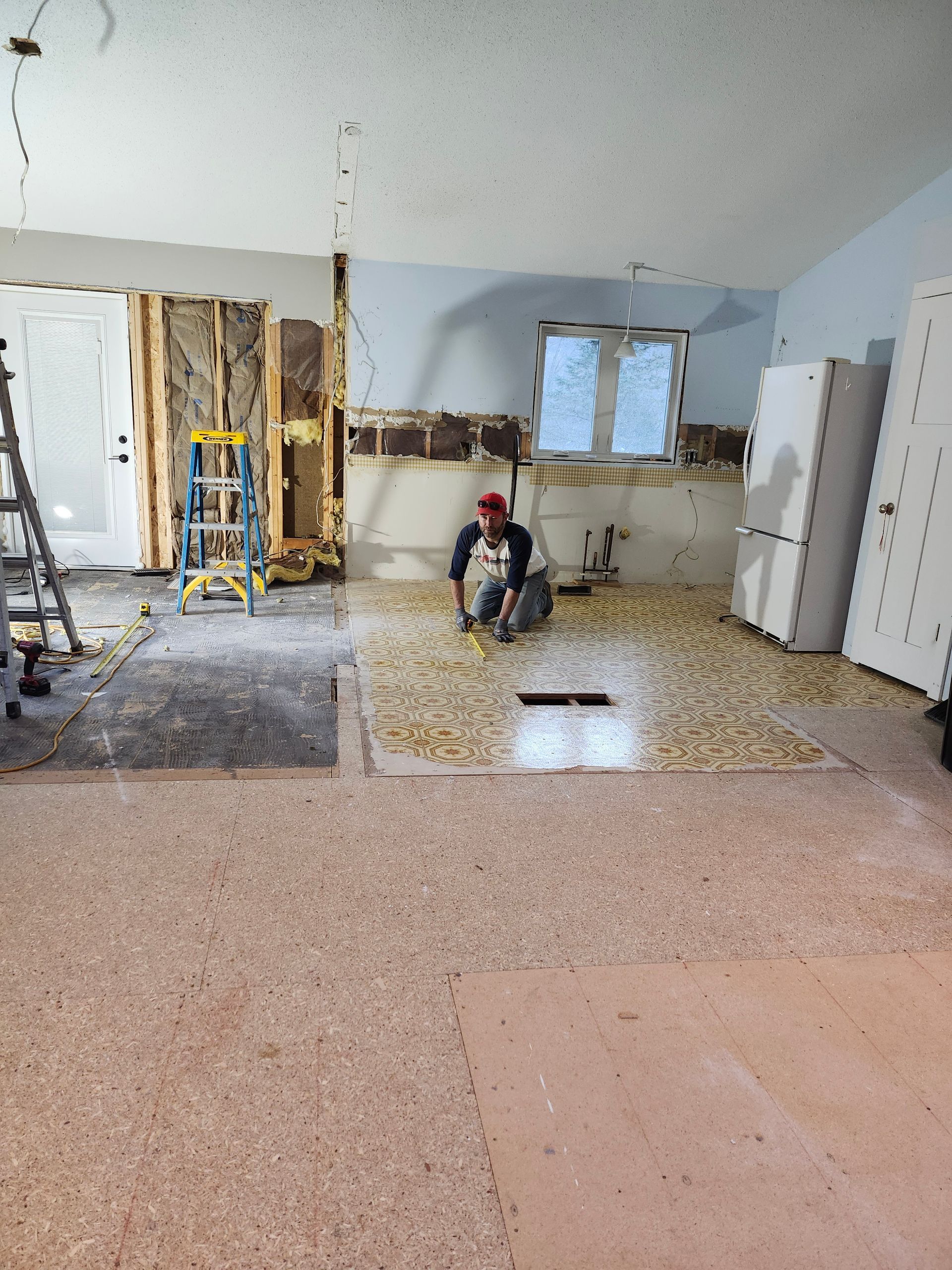 Kitchen under renovation with exposed wall studs, tools, and a worker kneeling on the floor