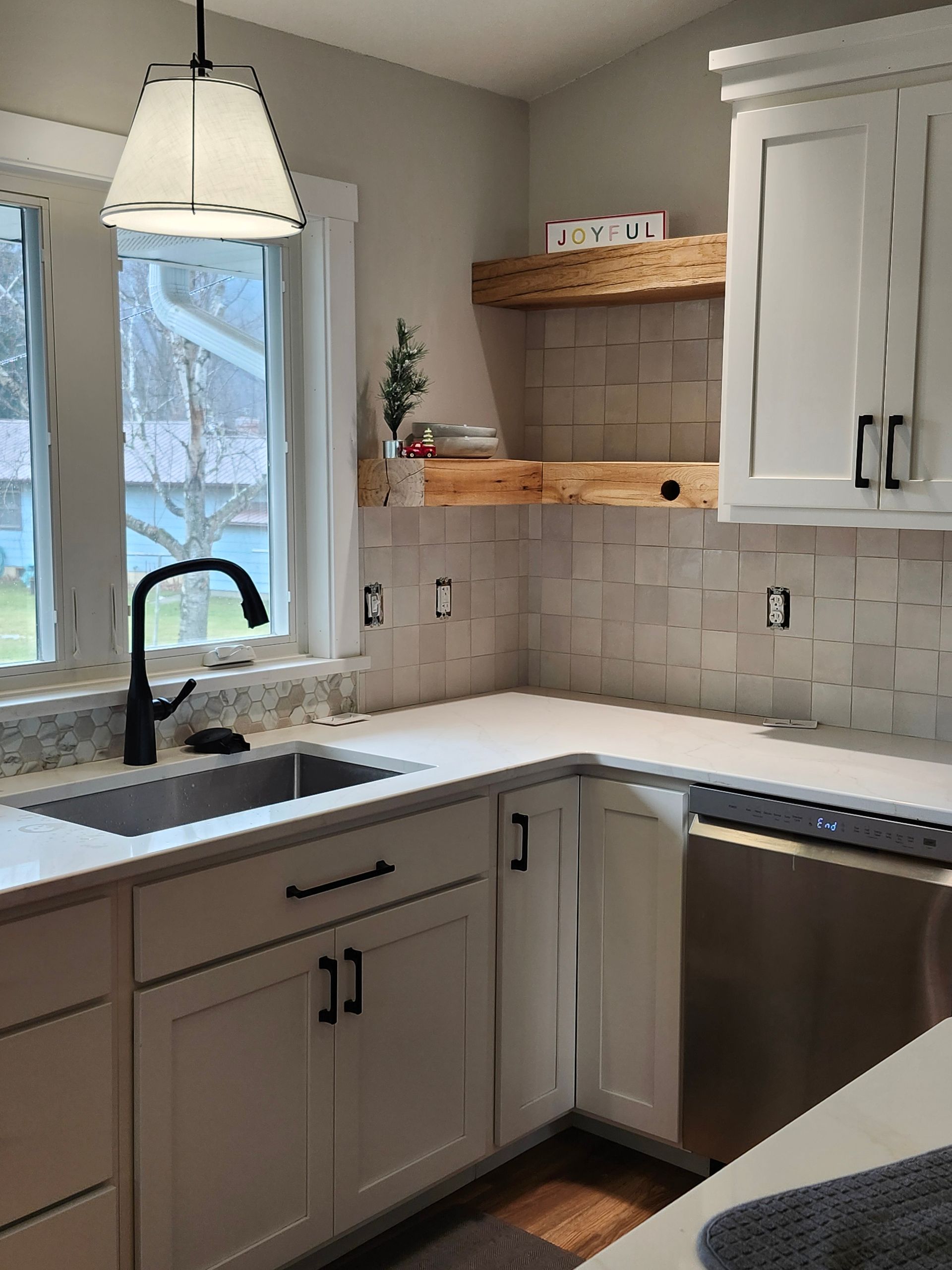 Modern kitchen corner with white cabinets, granite sink, window, and stainless dishwasher.