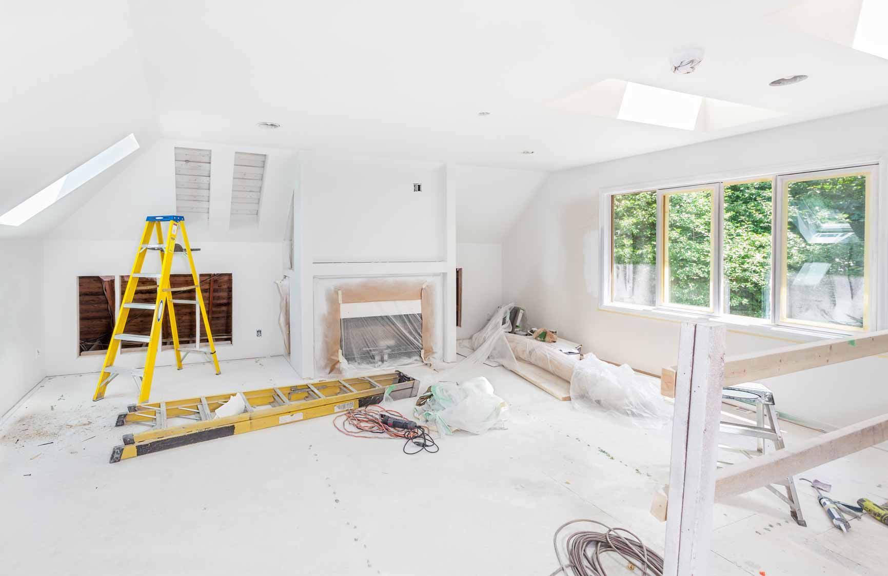Bright white room under renovation with ladder, fireplace, tools, and large windows.