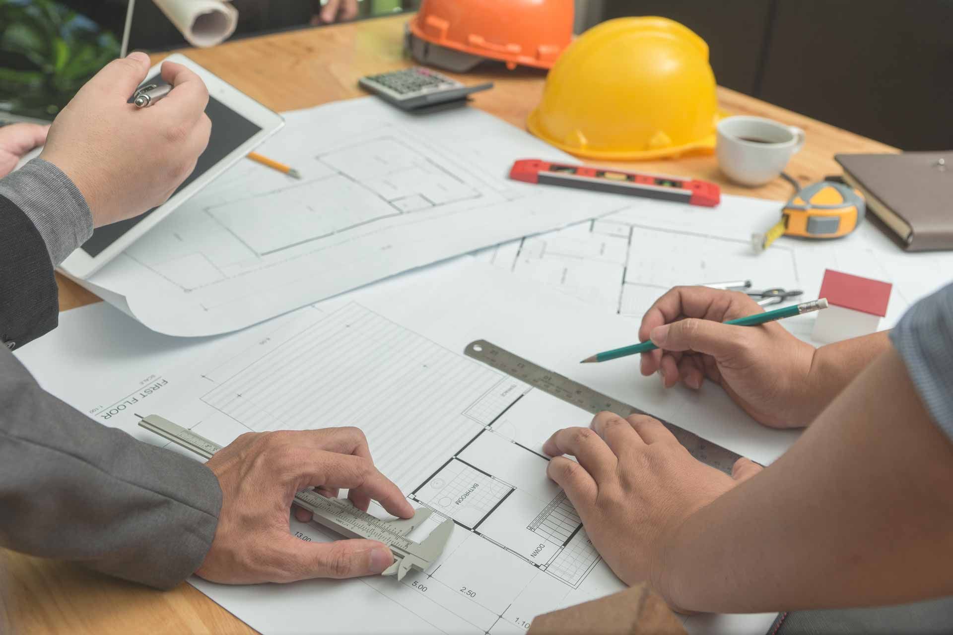 Team reviewing blueprints around a table with a yellow hard hat, ruler, and coffee cup