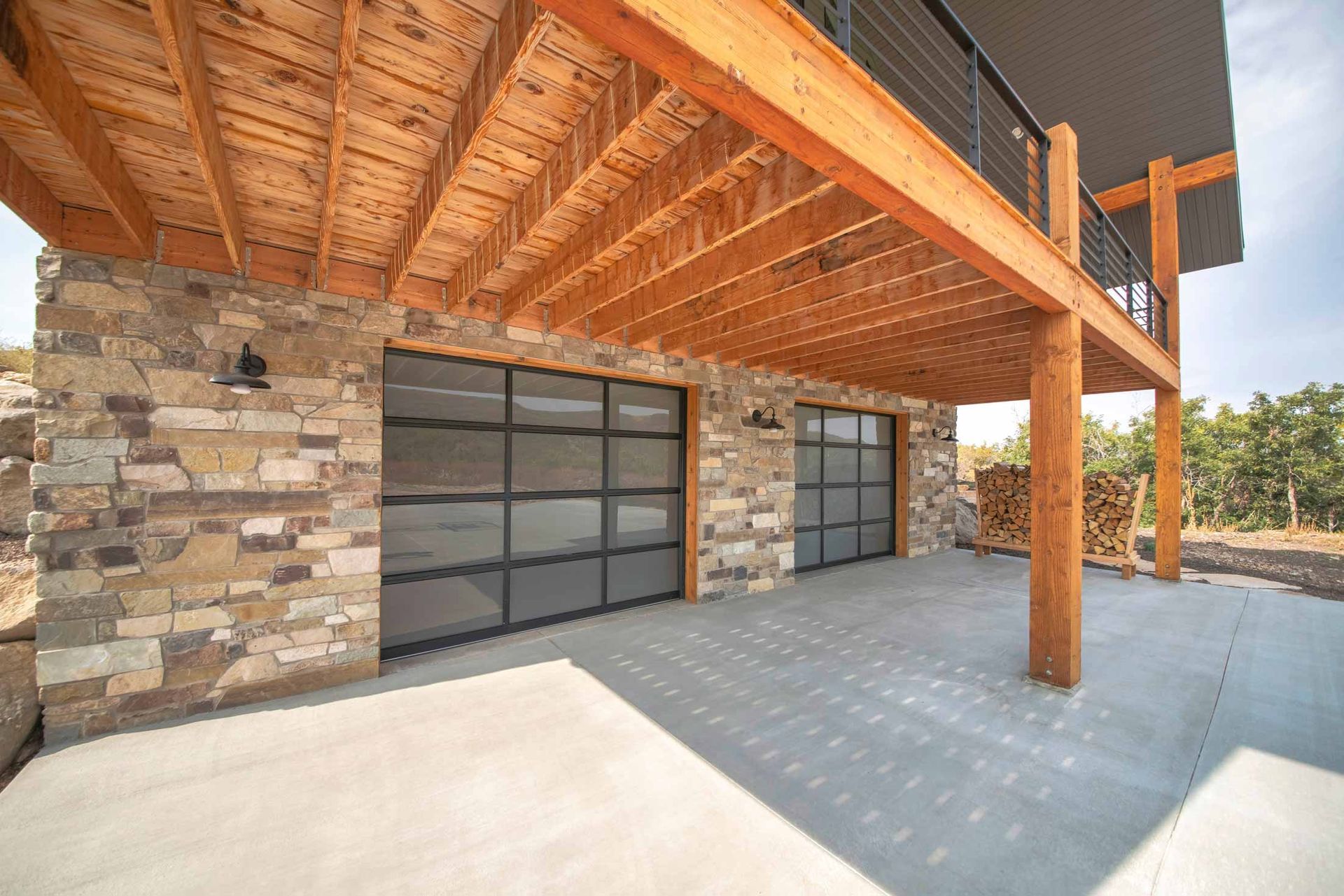 Modern stone-and-wood house exterior with large glass garage doors and a covered patio