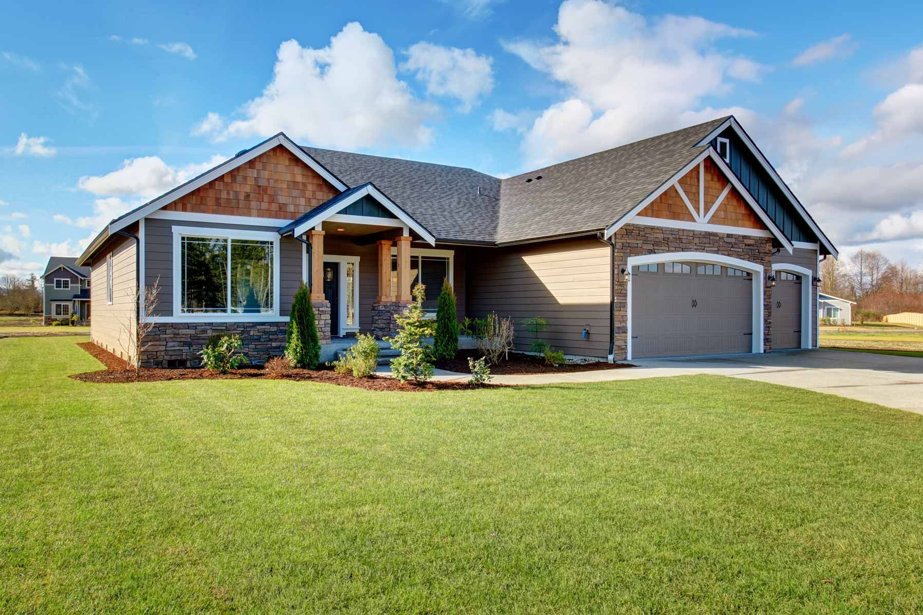 Single-story brick house with attached garage and a large green lawn under a blue sky