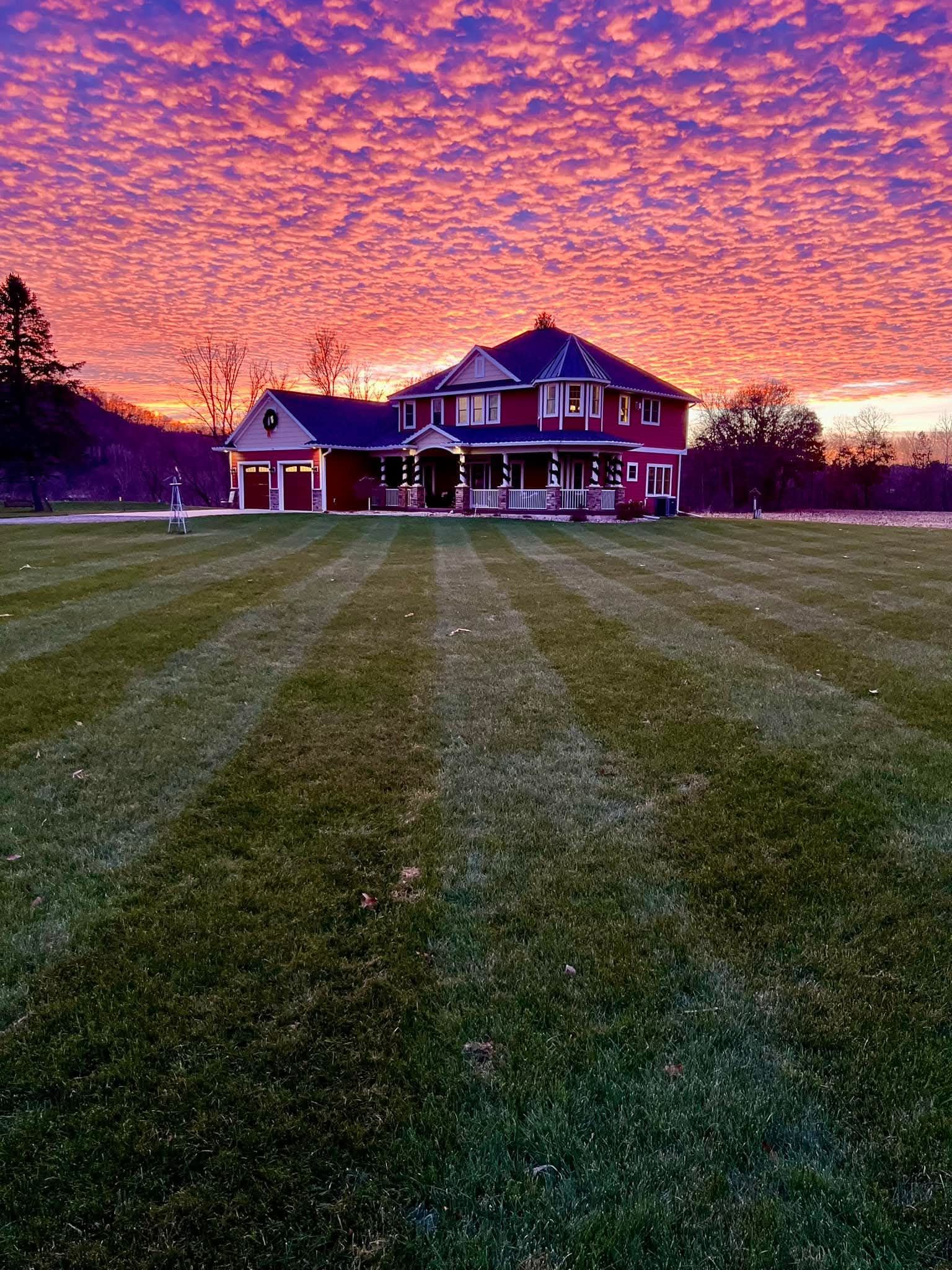 Large house at sunset beneath a pink-purple sky, seen across a wide grassy field.